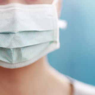 young woman in medical face protection mask indoors on blue background. Sick person