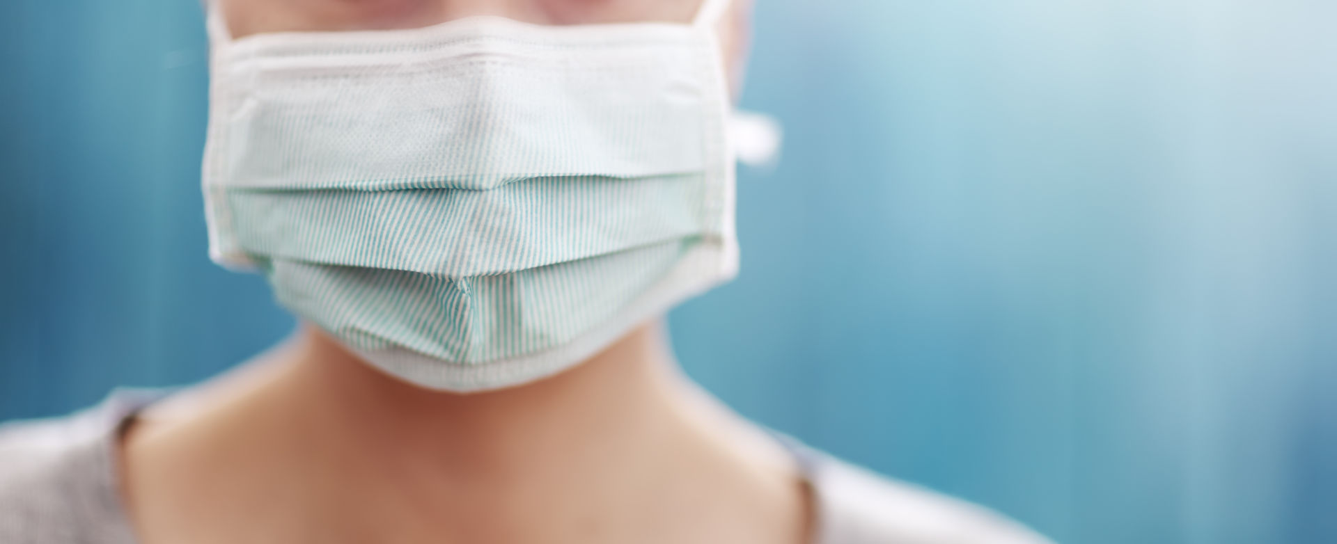 young woman in medical face protection mask indoors on blue background young woman in medical face protection mask indoors on blue background. Sick person