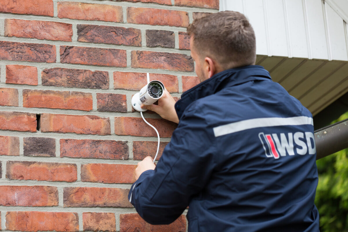 WSD Sicherheitsmitarbeiter installiert &Uuml;berwachungskamera an Hauswand zur Einbruchpr&auml;vention